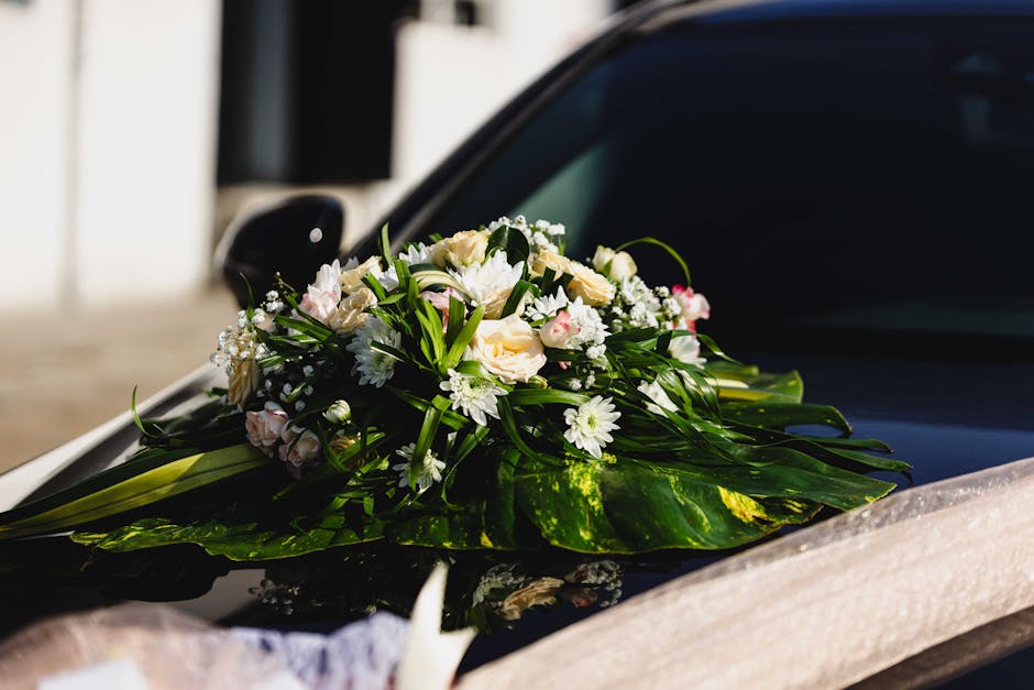 A floral bouquet arranged with white roses, small white daisies, and delicate baby's breath, accented by lush green foliage and long leaves. The flowers are fresh with soft petals and sturdy stems, ar